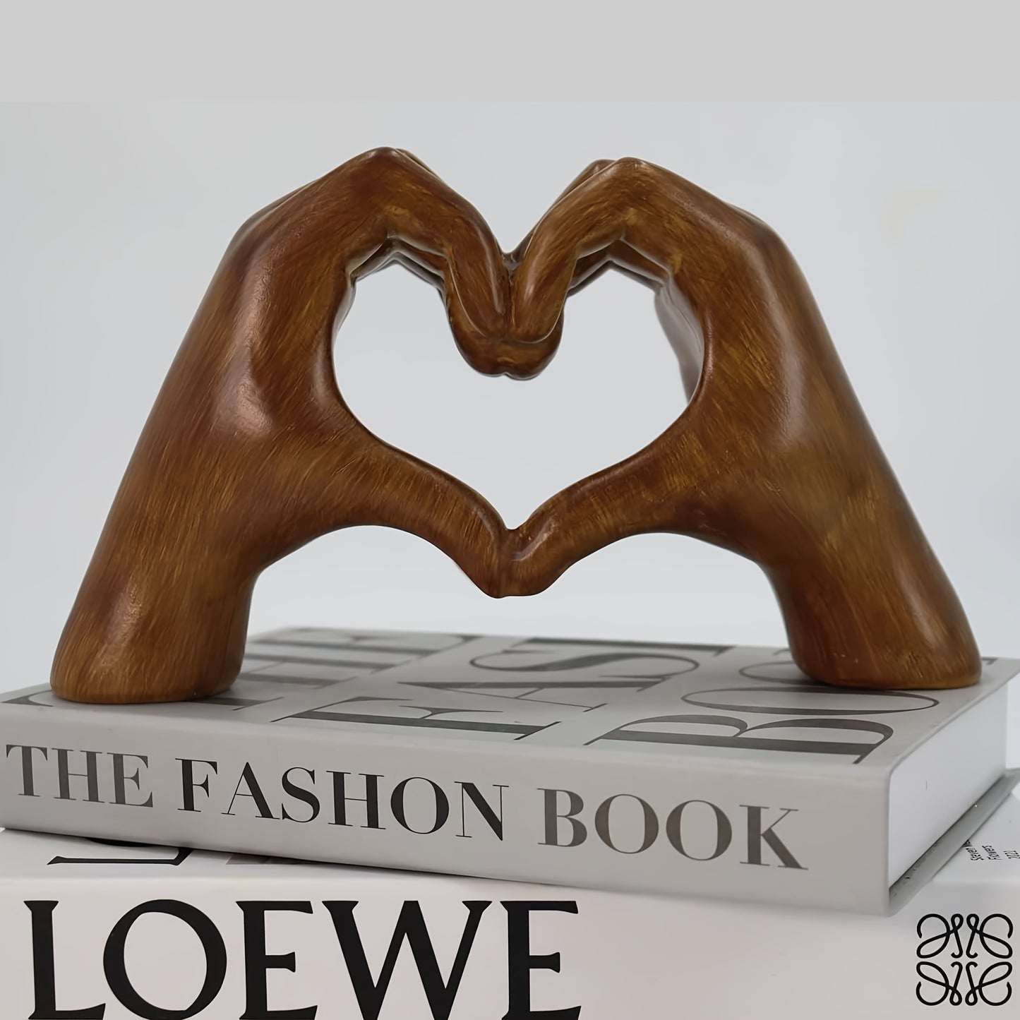 Heart-shaped resin sculpture decor by Nutshell made of brown hands forming a heart resting on fashion books