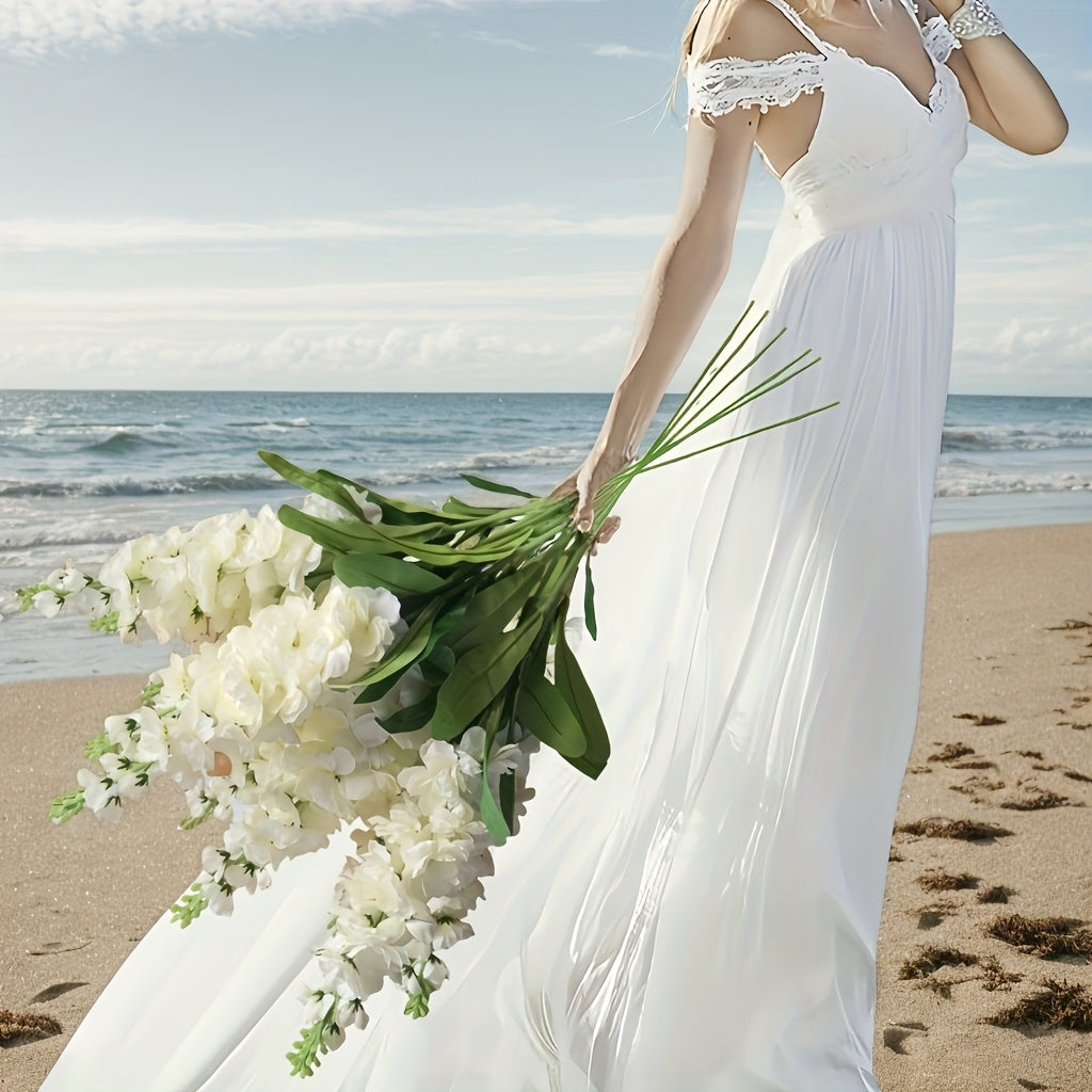 Large outdoor artificial delphinium bouquet held by a woman in a flowing white dress on the beach