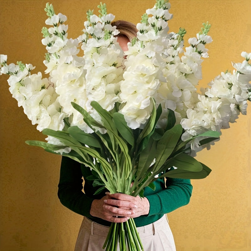 Large outdoor artificial delphinium in white held by a person against a yellow background