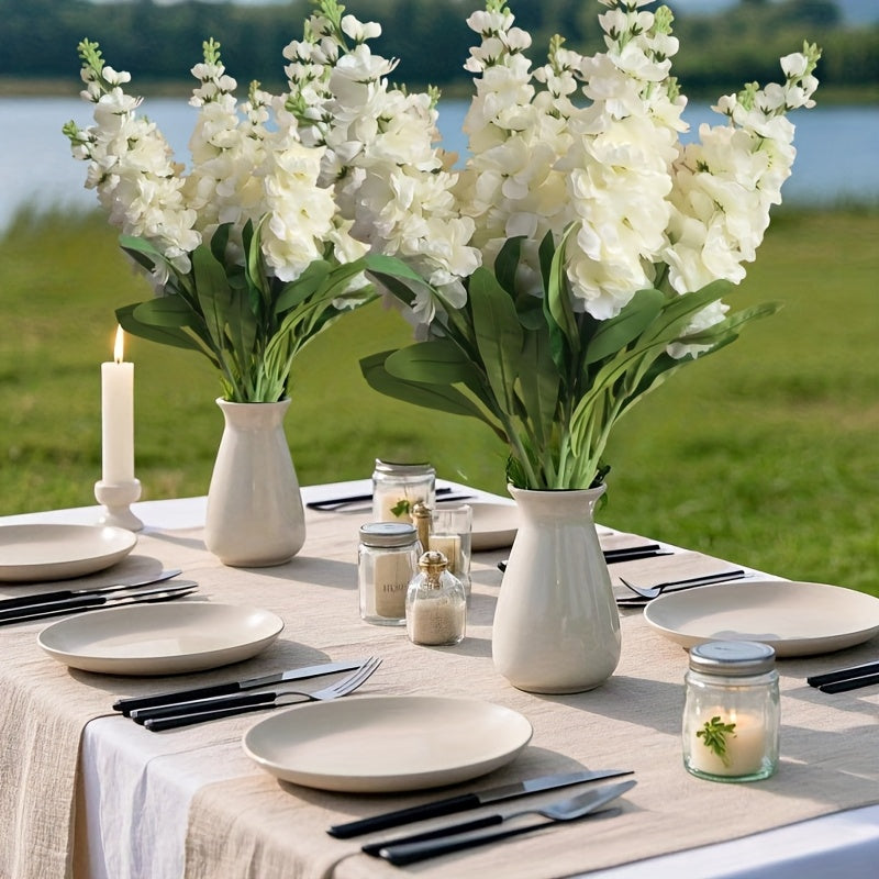 Two large outdoor artificial delphinium arrangements in white vases on a dining table by the water