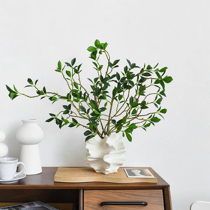 Nordic art coral vase by Nutshell with ruffled design holding green leafy branches on wooden table