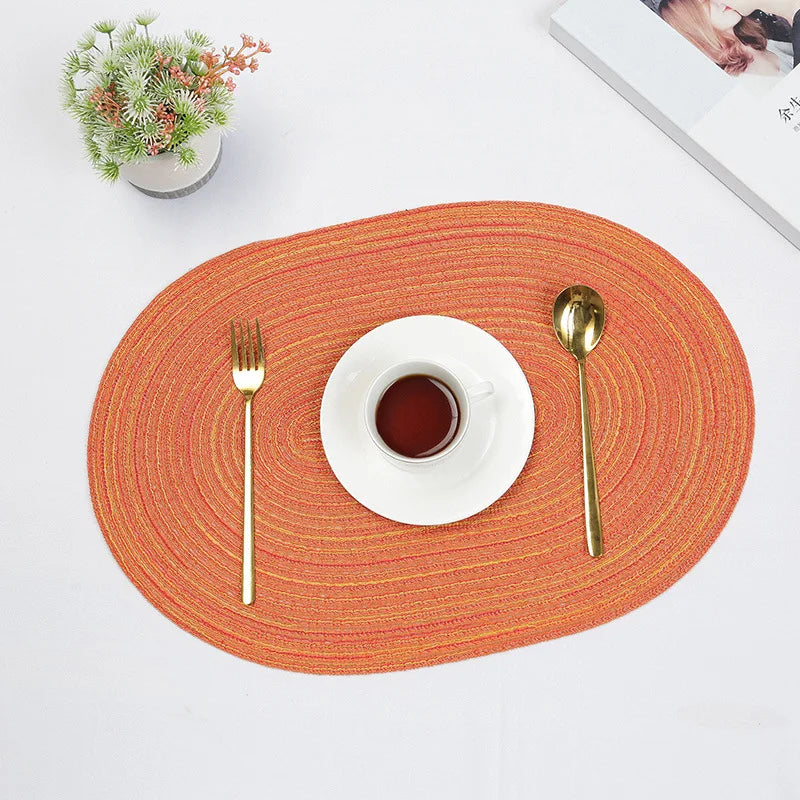 Oval Braided Placemats in vibrant orange with a cup and cutlery set for stylish dining