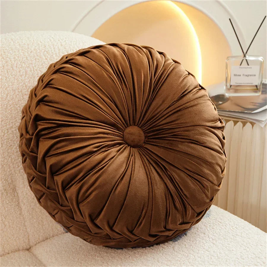 Nutshell round pumpkin pillow in brown velvet fabric placed on a white textured chair
