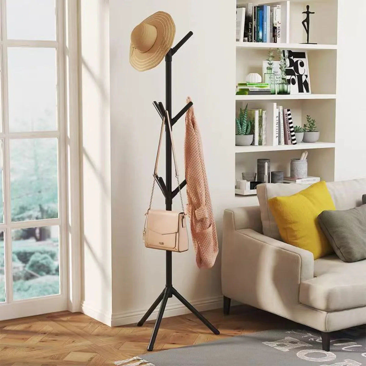 Nutshell black tree branch coat rack in living room with hat handbag and scarf beside sofa and window