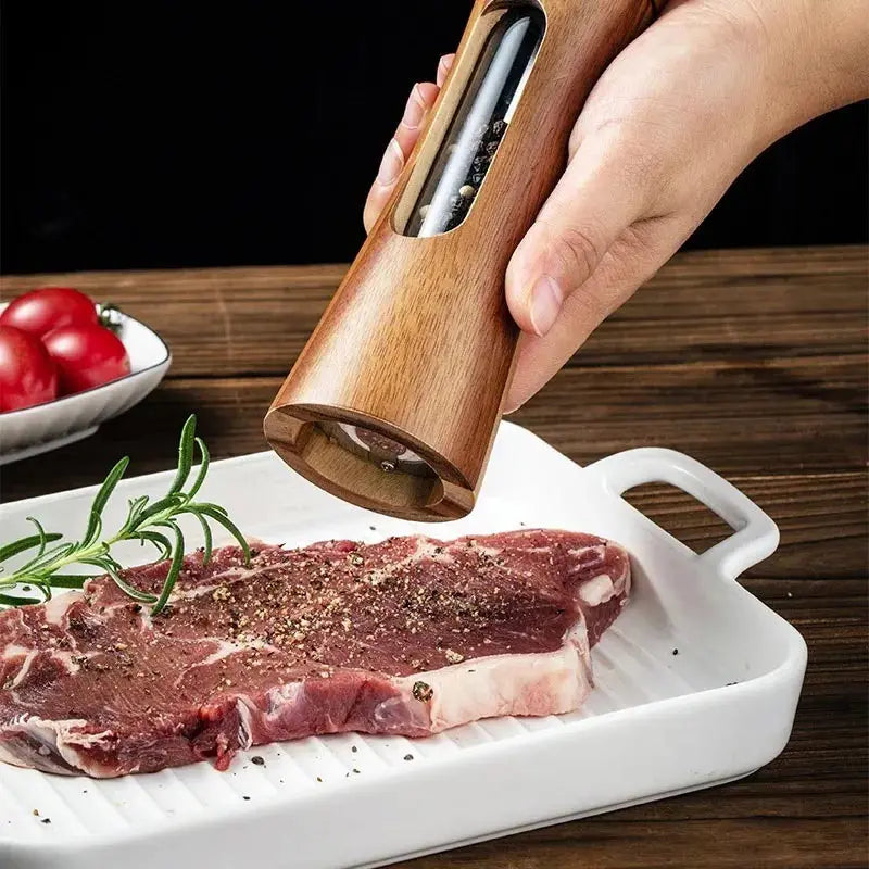Hand seasoning raw steak with wooden salt and pepper grinder set on white grill pan