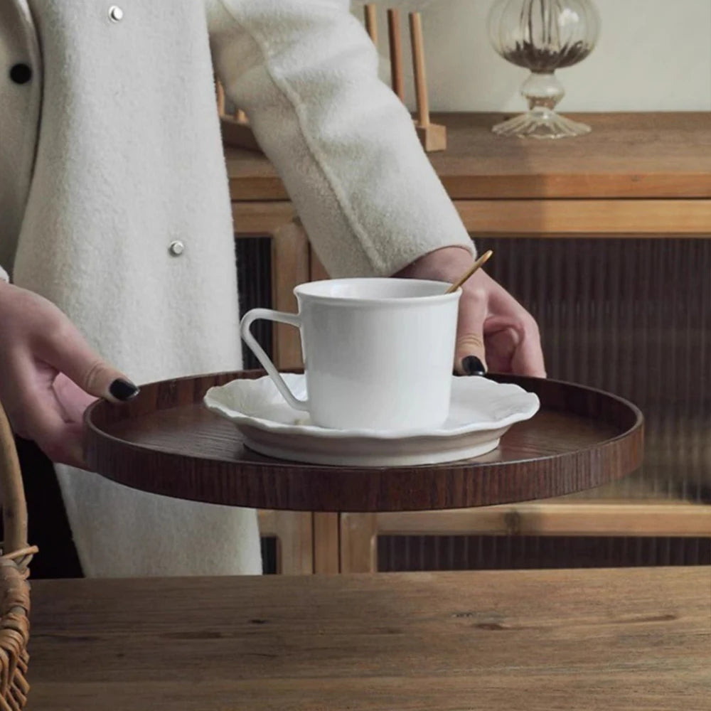 Nutshell wooden serving tray holding a white cup and saucer held by a person in a cozy setting