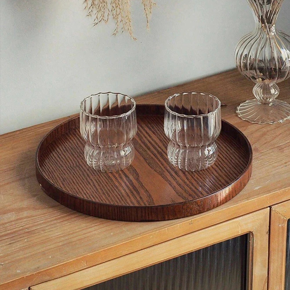 Nutshell round wooden serving tray with two textured glass cups on wooden cabinet