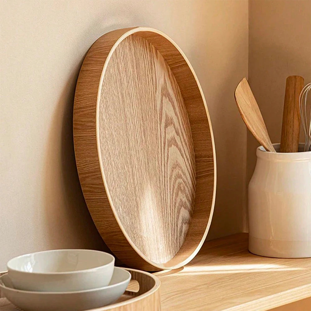 Nutshell round wooden serving tray with natural grain resting on wooden shelf near kitchen utensils