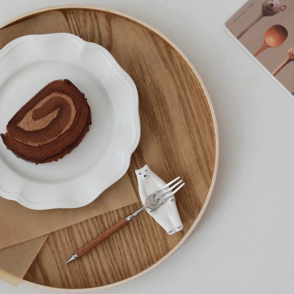 Nutshell wooden serving tray with a white plate holding a chocolate roll and a wooden-handled fork on a white cat-shaped rest