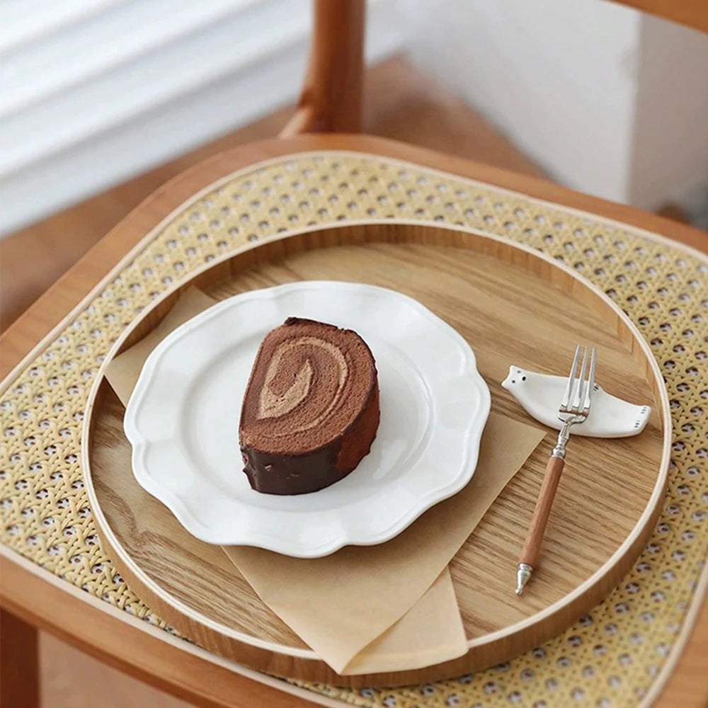 Nutshell wooden serving tray with a white plate holding a chocolate cake roll and a fork on a woven chair