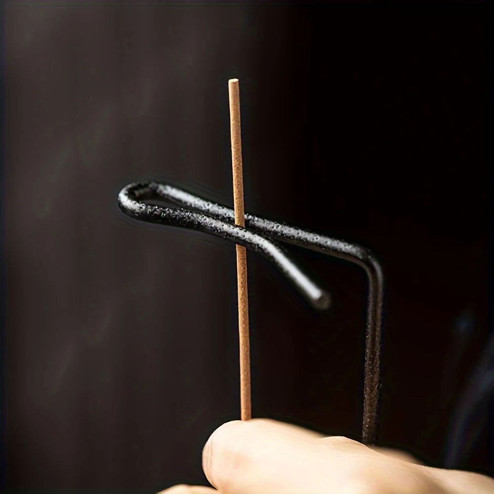 Nutshell black metal anti-ash incense burner holding a burning incense stick against a dark background