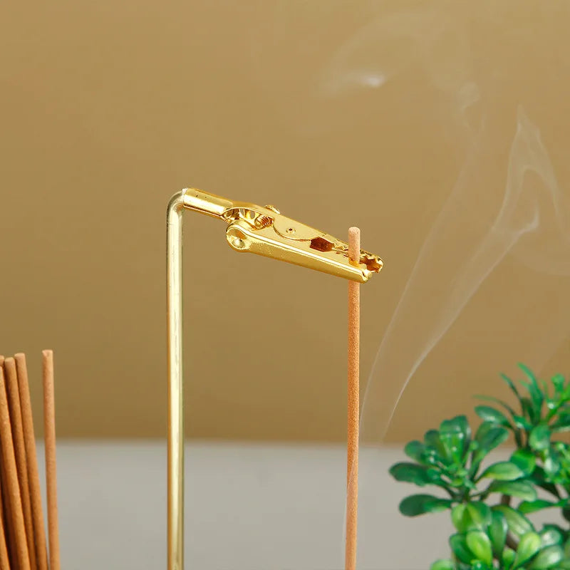 Nutshell anti-ash incense holder with storage featuring a gold clip holding a burning incense stick with smoke rising