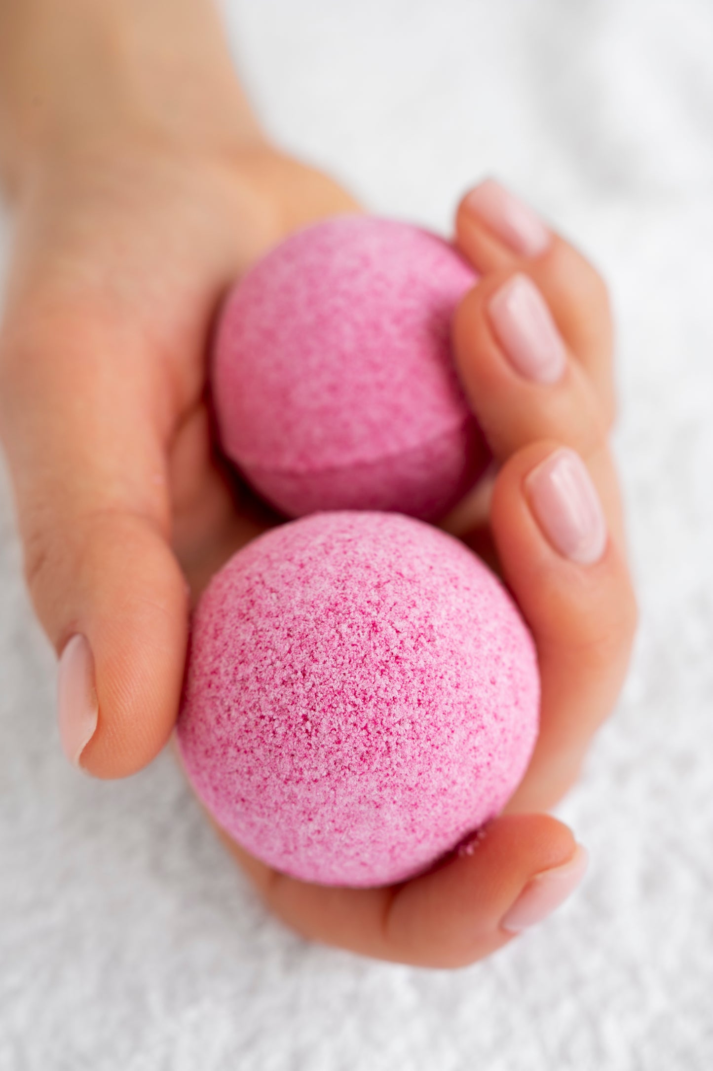 Nutshell Bath Fizz Bon Bon in pink, held in a hand for a relaxing bath experience