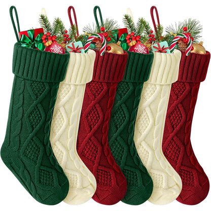 Set of cable knit Christmas stockings in green, red, and cream with festive decorations on top