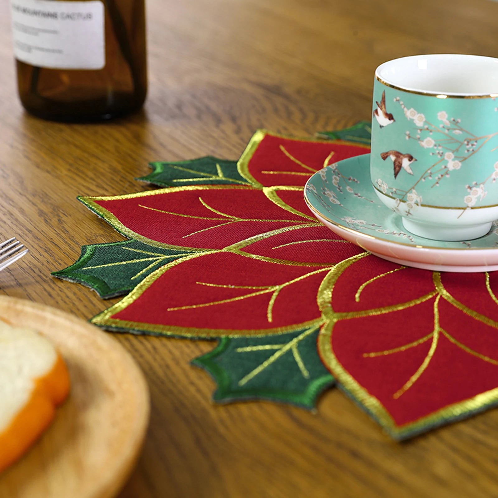 Christmas holly leaf placemat in red and green with tea cup and sliced bread on wooden table