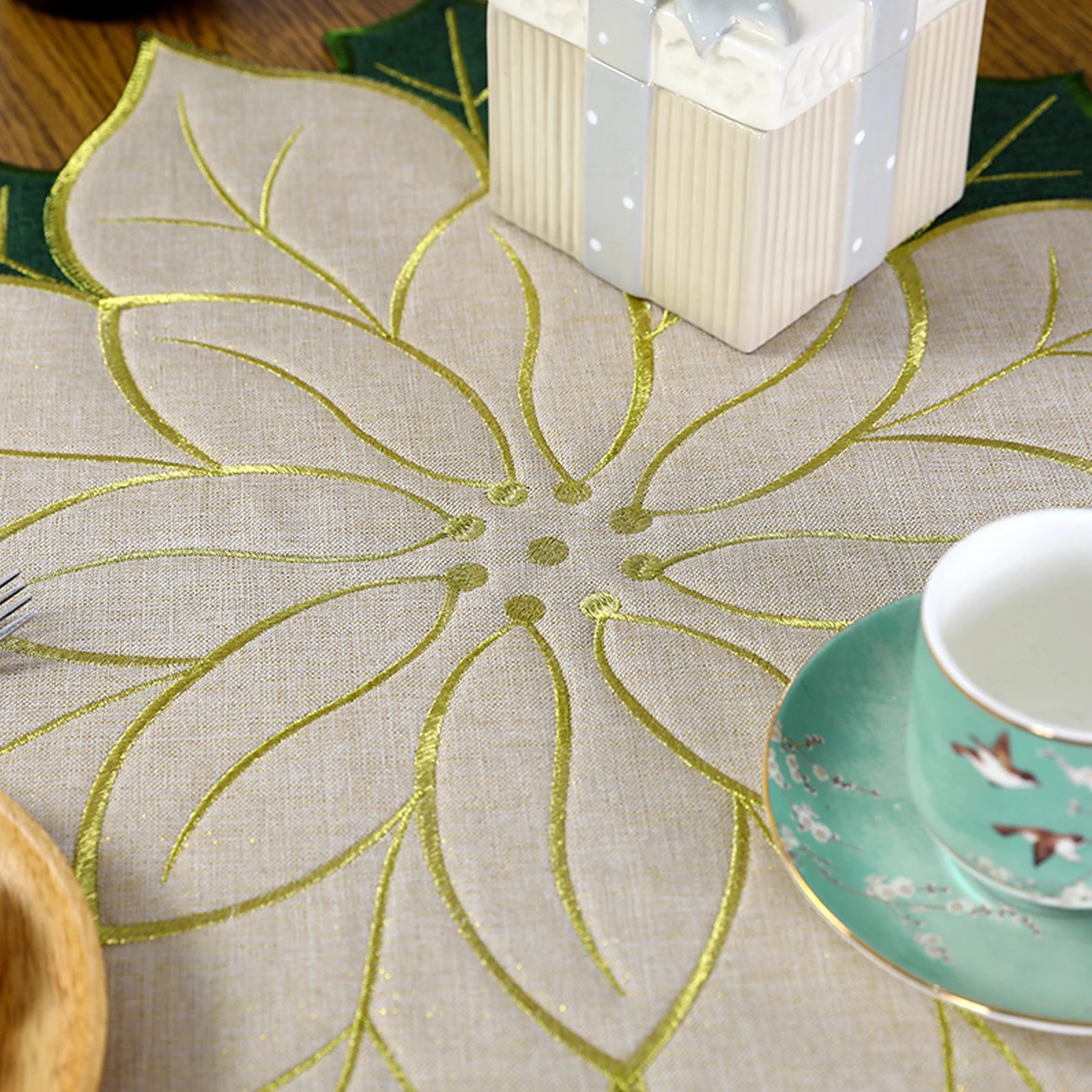 Elegant Christmas holly leaf placemat in gold and green with a decorative setting of dishes and a gift box