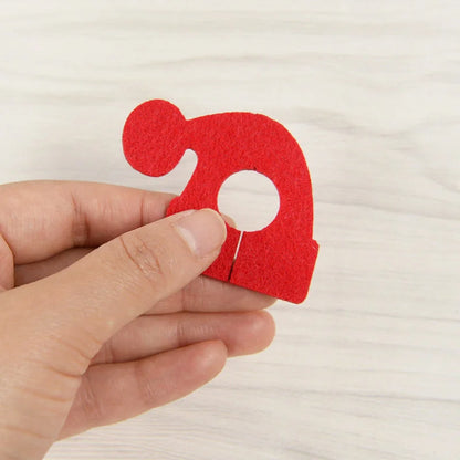 Hand holding a red felt Christmas wine glass charms set featuring a festive Santa hat design