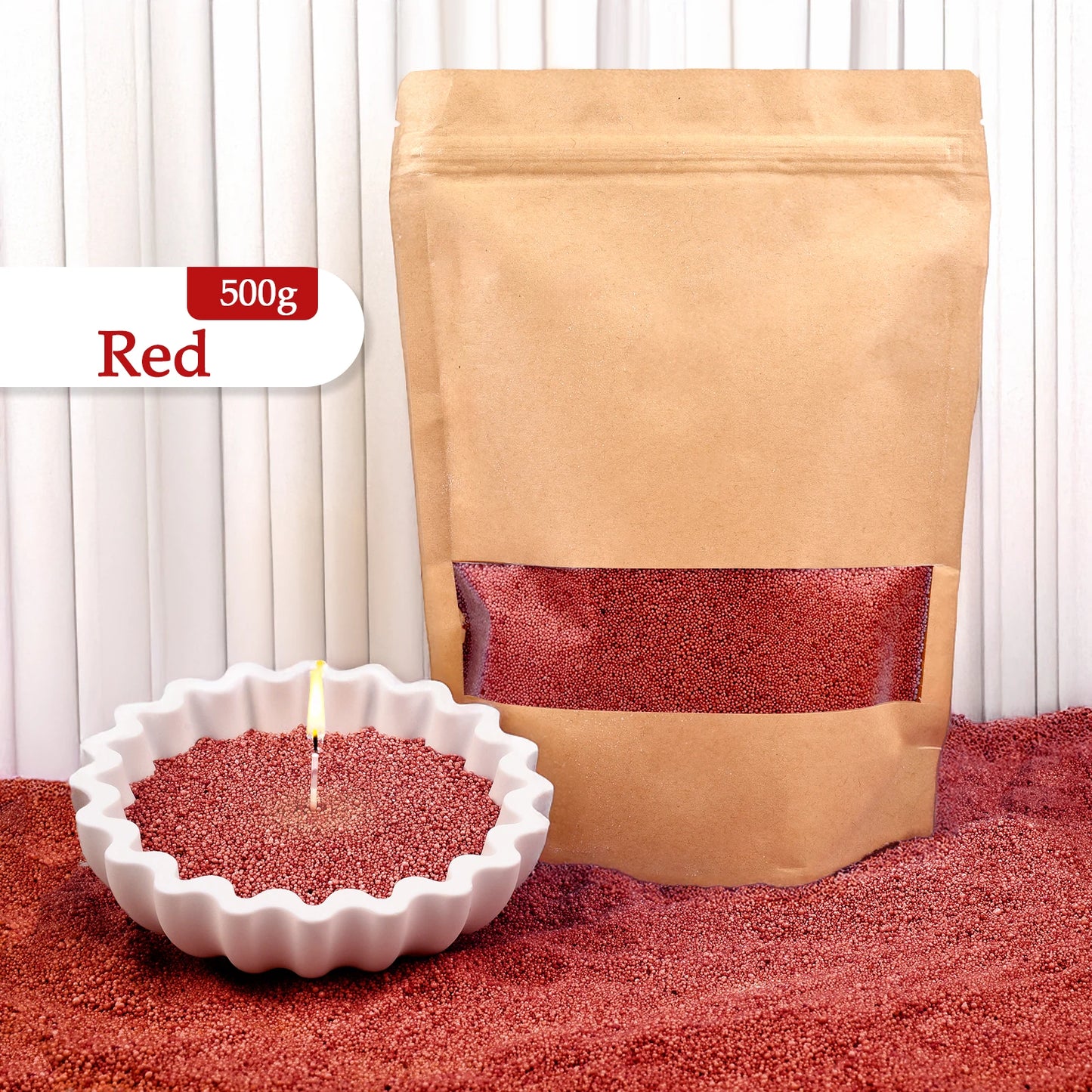 Nutshell red colored candle sand 500g in a brown resealable bag with a lit candle in white scalloped dish