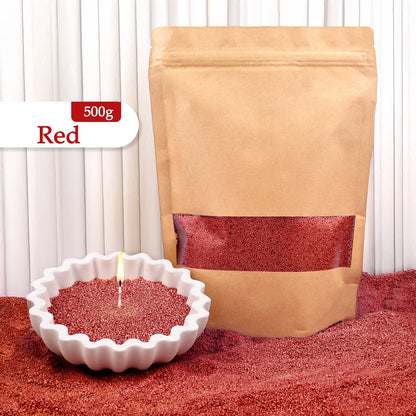 Nutshell red colored candle sand 500g in a brown resealable bag with a lit candle in white scalloped dish