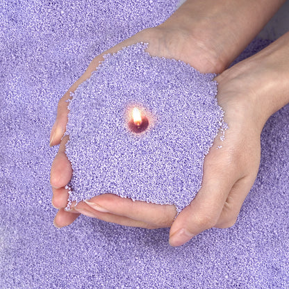 Hands holding lit candle surrounded by purple colored candle sand by Nutshell