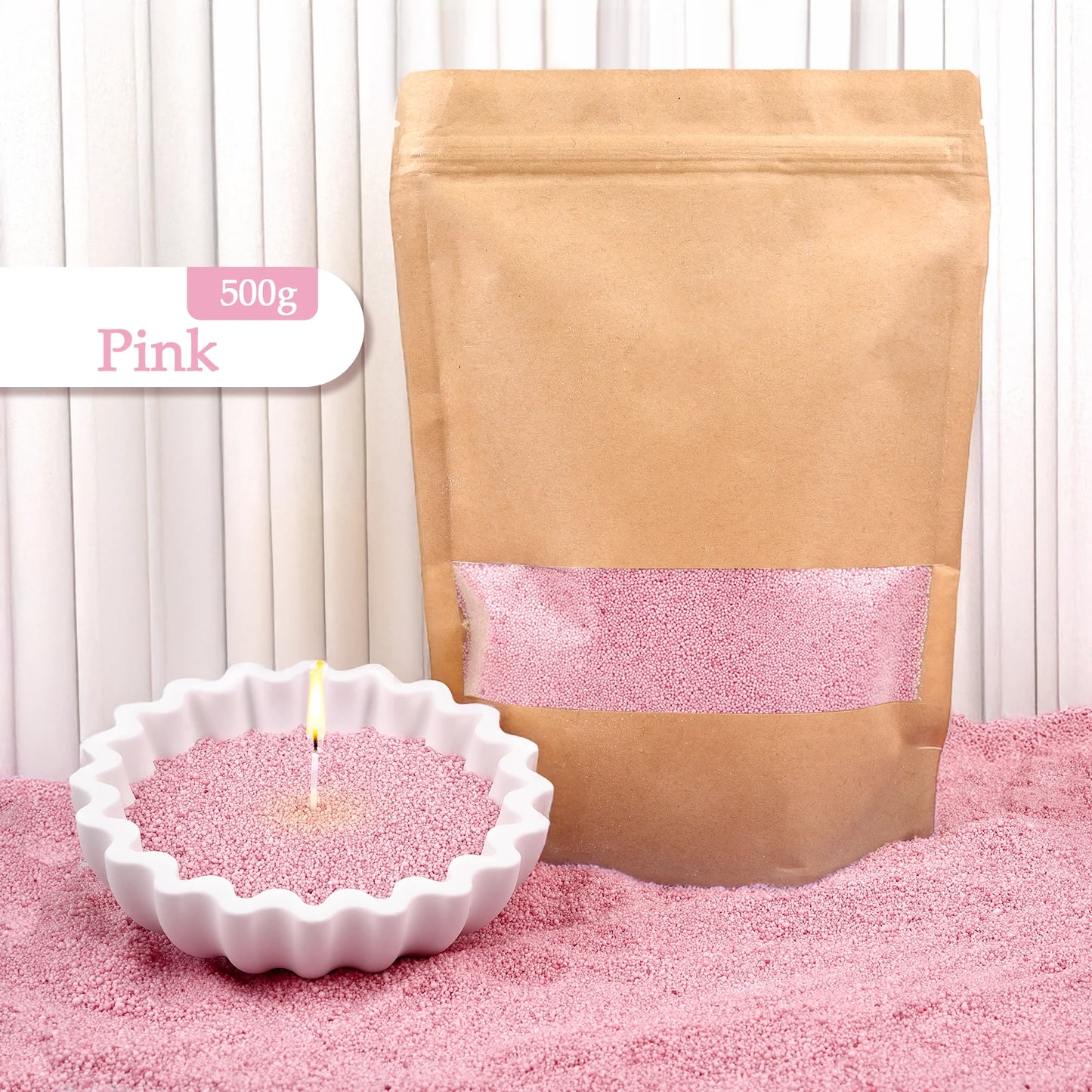 Nutshell pink colored candle sand 500g in resealable brown pouch with lit candle in white scalloped dish