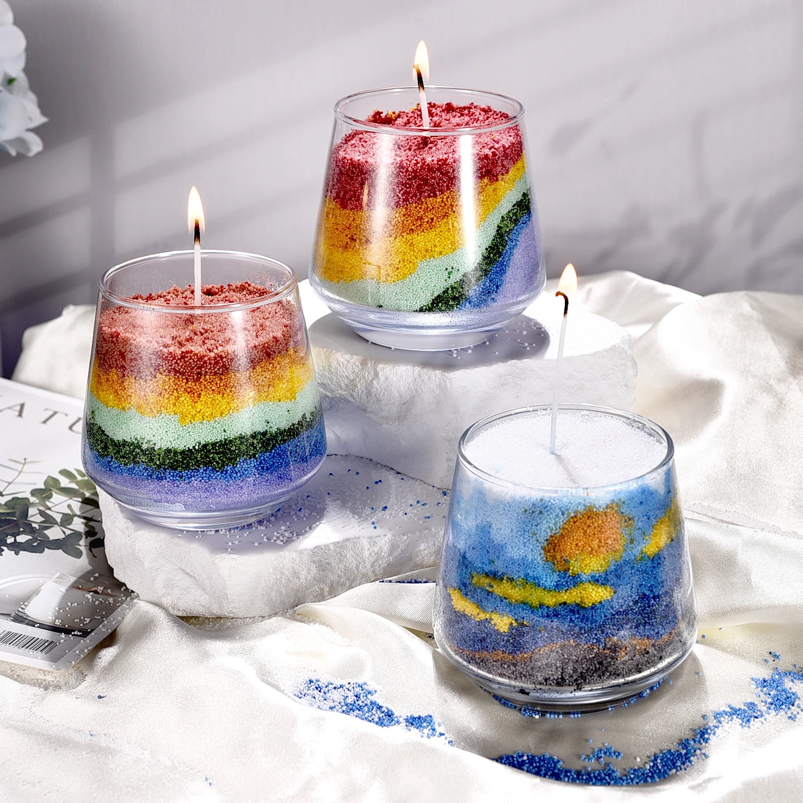 Nutshell candles made with vibrant layers of colored candle sand in clear glass containers with lit wicks