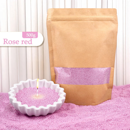 Nutshell rose red colored candle sand 500g in brown resealable bag with lit candle in white ceramic holder
