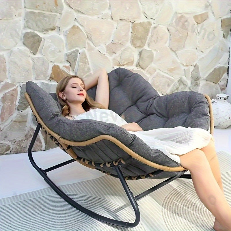 Woman reclining on a large gray comfortable patio chair cushion on a rattan framed rocking lounger outdoors