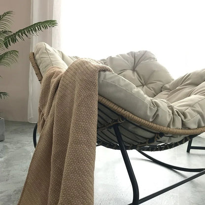 Nutshell lazy leisure rocking chair with cushion beige tufted seat on wicker frame with black metal rockers and tan throw