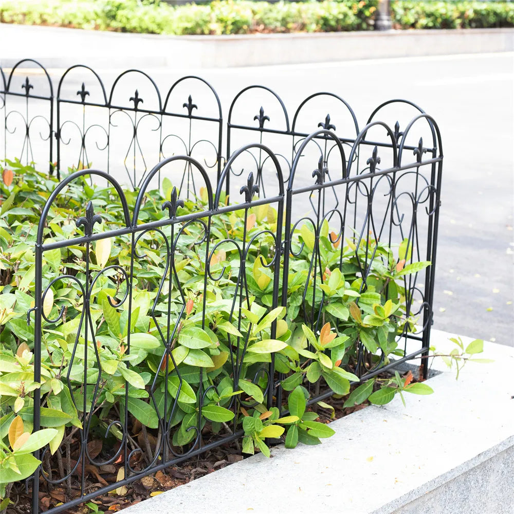 Nutshell black metal decorative garden fence panels surrounding leafy green plants along a concrete edge