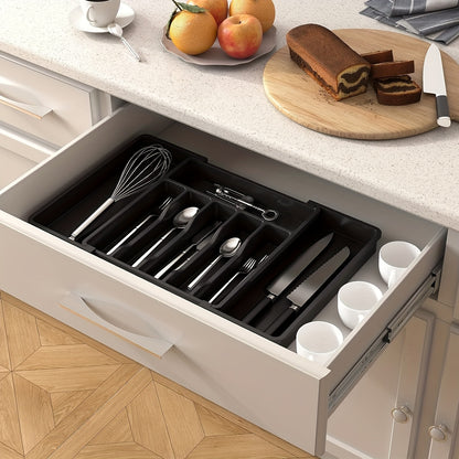 Nutshell expandable cutlery tray neatly organizing utensils in a kitchen drawer with fruits and cake on the countertop