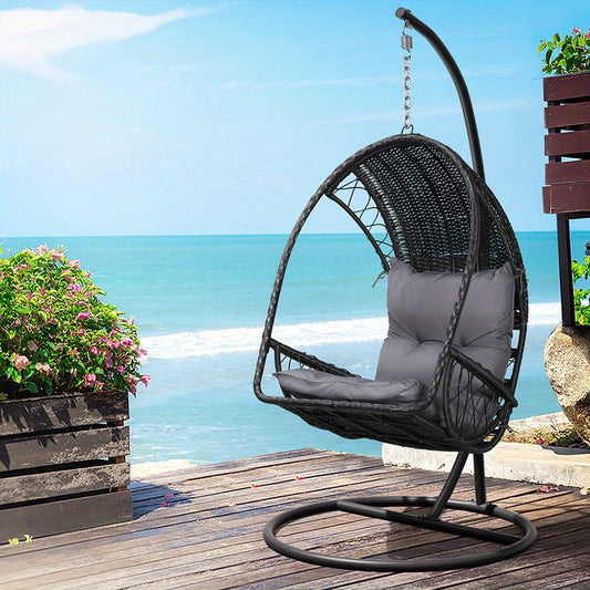 Nutshell outdoor egg chair hammock in black rattan with gray cushion on metal stand on seaside deck