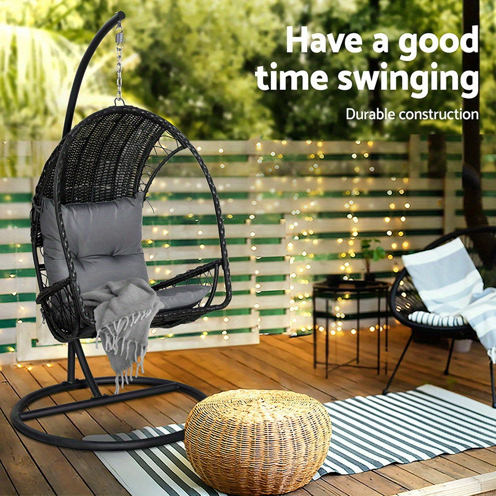 Nutshell outdoor egg chair hammock in black wicker with gray cushion on a deck with rattan ottoman and string lights