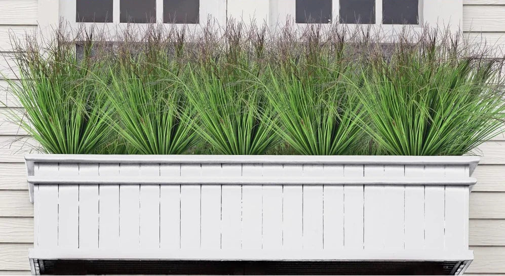 Nutshell Faux onion grass artificial plant in white window box planter beneath exterior windows on siding