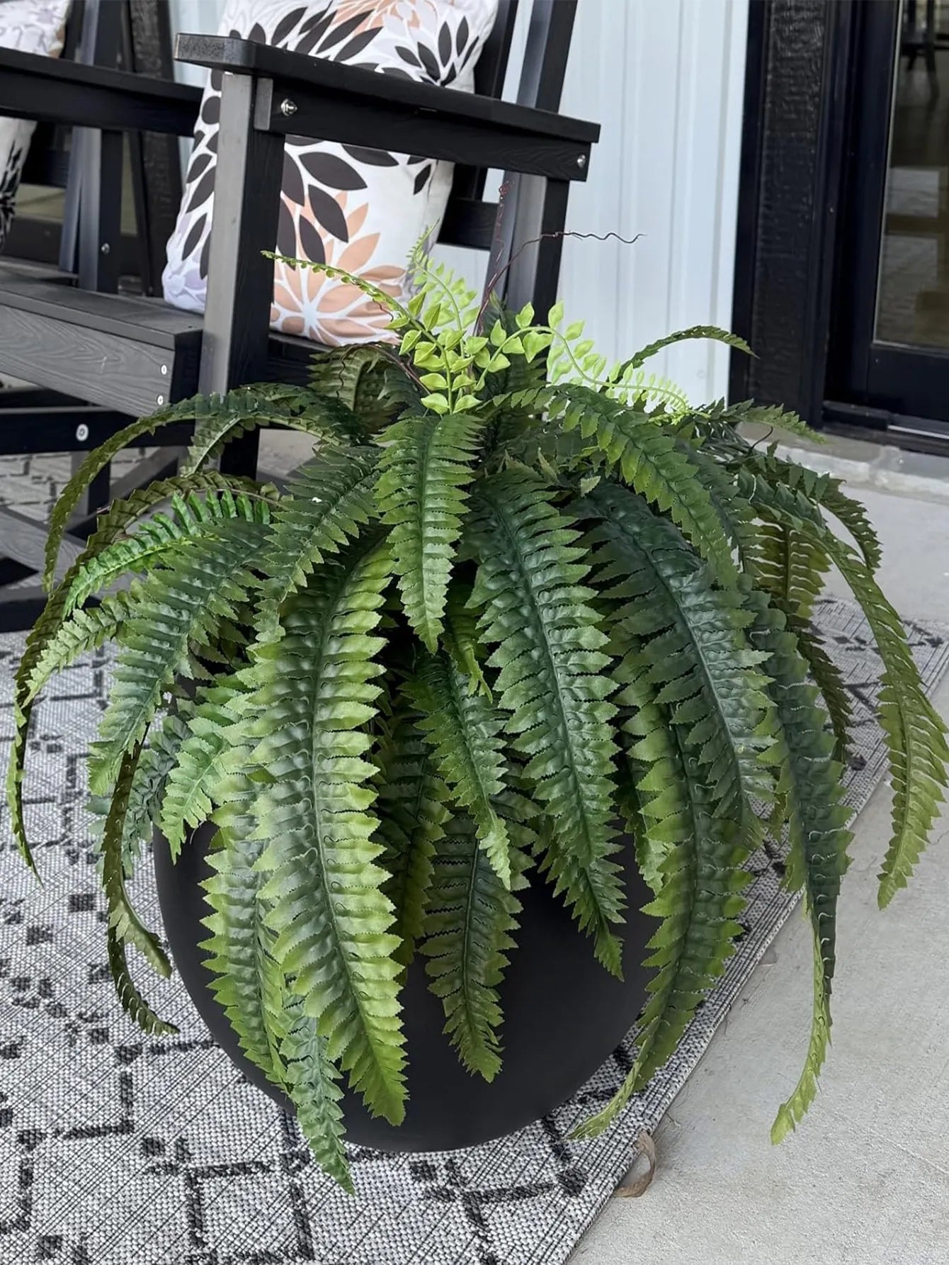 Nutshell artificial fern hanging plant in black planter draping over patio pot near outdoor chair