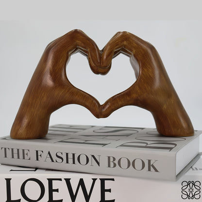 Heart-shaped resin sculpture decor by Nutshell made of brown hands forming a heart resting on fashion books