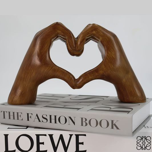 Heart-shaped resin sculpture decor by Nutshell made of brown hands forming a heart resting on fashion books