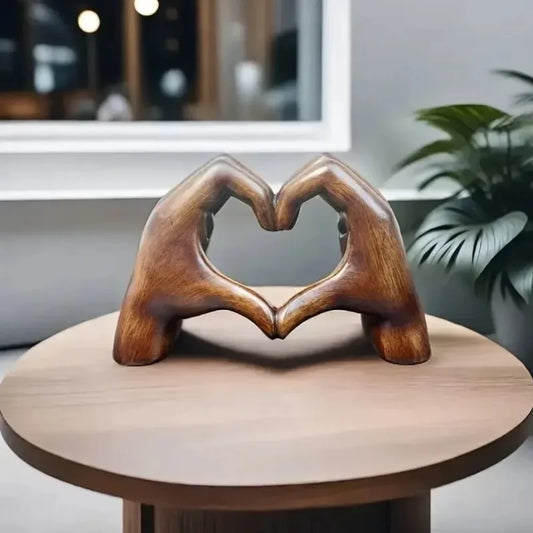 Heart-shaped resin sculpture decor depicting two hands forming a heart on a wooden table