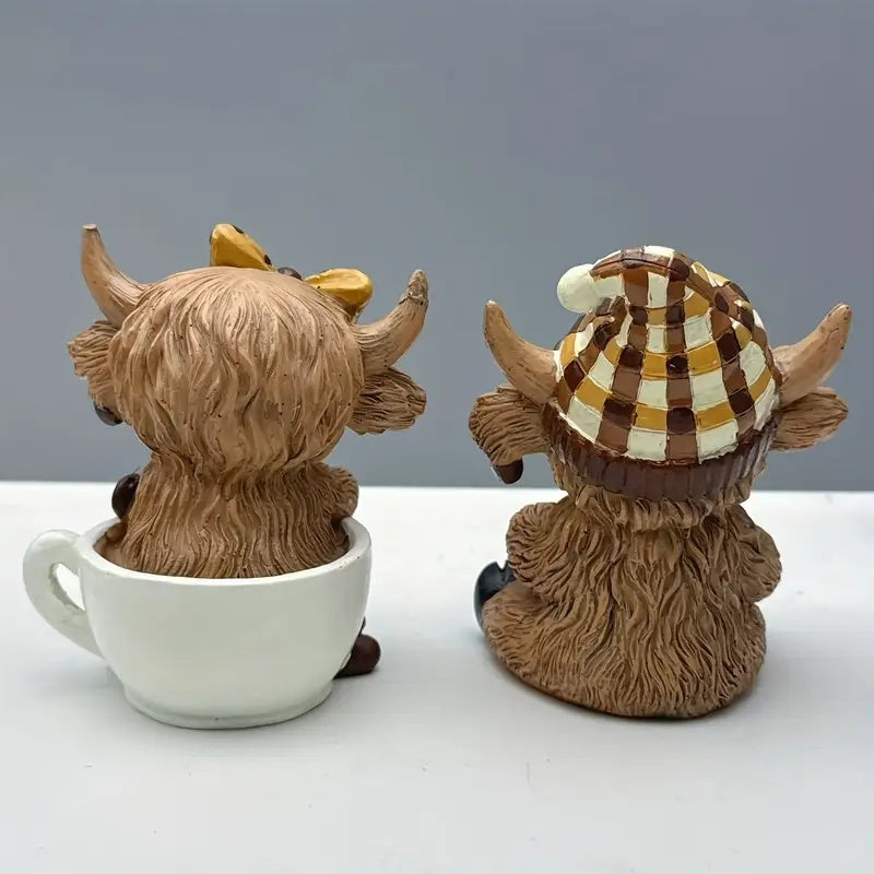 Adorable highland cow coffee decor figurines featuring one with a yellow bow and the other in a striped hat