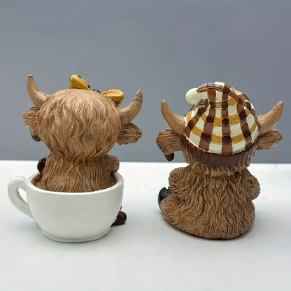 Adorable highland cow coffee decor figurines featuring one with a yellow bow and the other in a striped hat