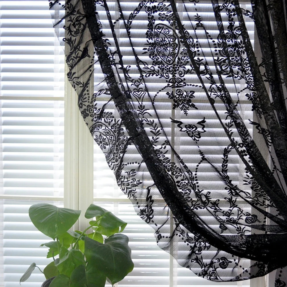 Black sheer curtain with floral medallion draped over white blinds with a green plant vintage voile ruffle lace drapes