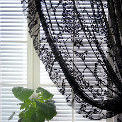 Black sheer curtain with floral medallion draped over white blinds with a green plant vintage voile ruffle lace drapes