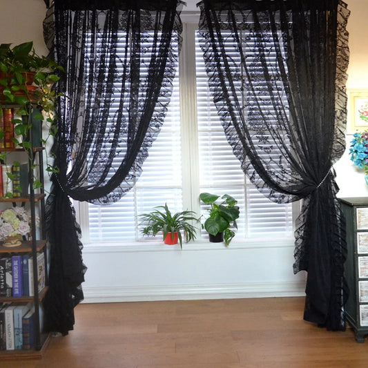 Black vintage voile ruffle lace drapes pulled back over white blinds framing a window with plants