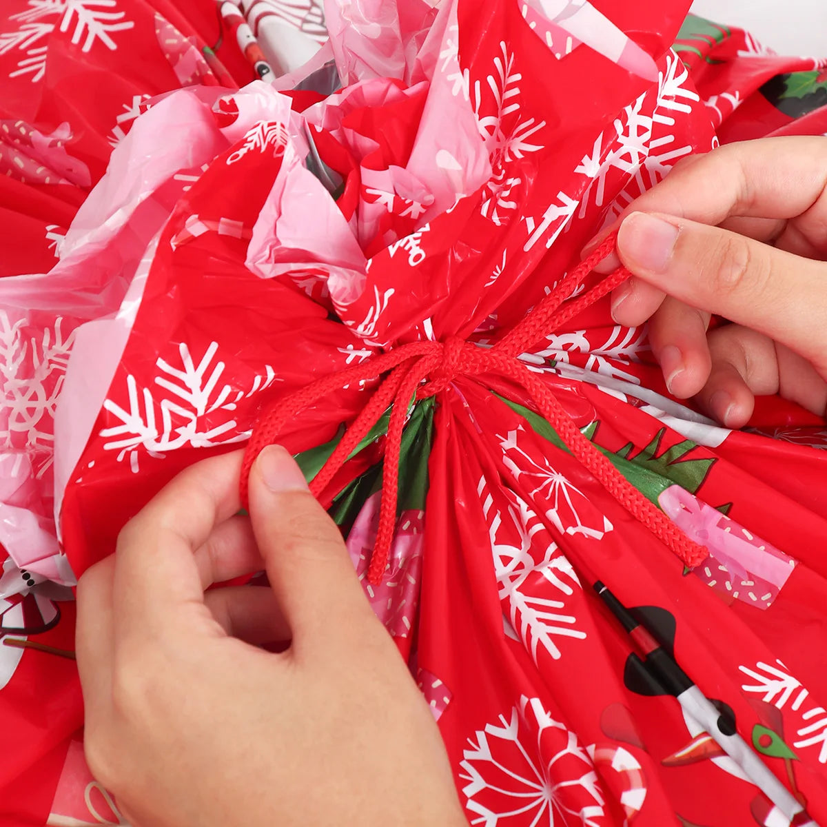 Two hands tying a large Christmas gift bags with festive holiday designs and snowflakes