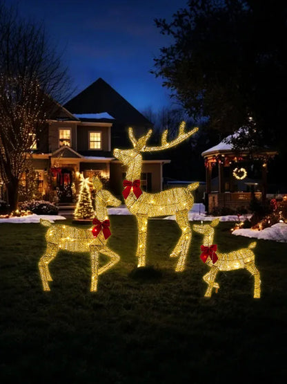 Lit outdoor Christmas deer decorations in a yard with festive bows and a decorated house in the background