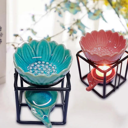 Porcelain lotus essential oil burner by Nutshell in teal and pink with black metal stands and lit candle