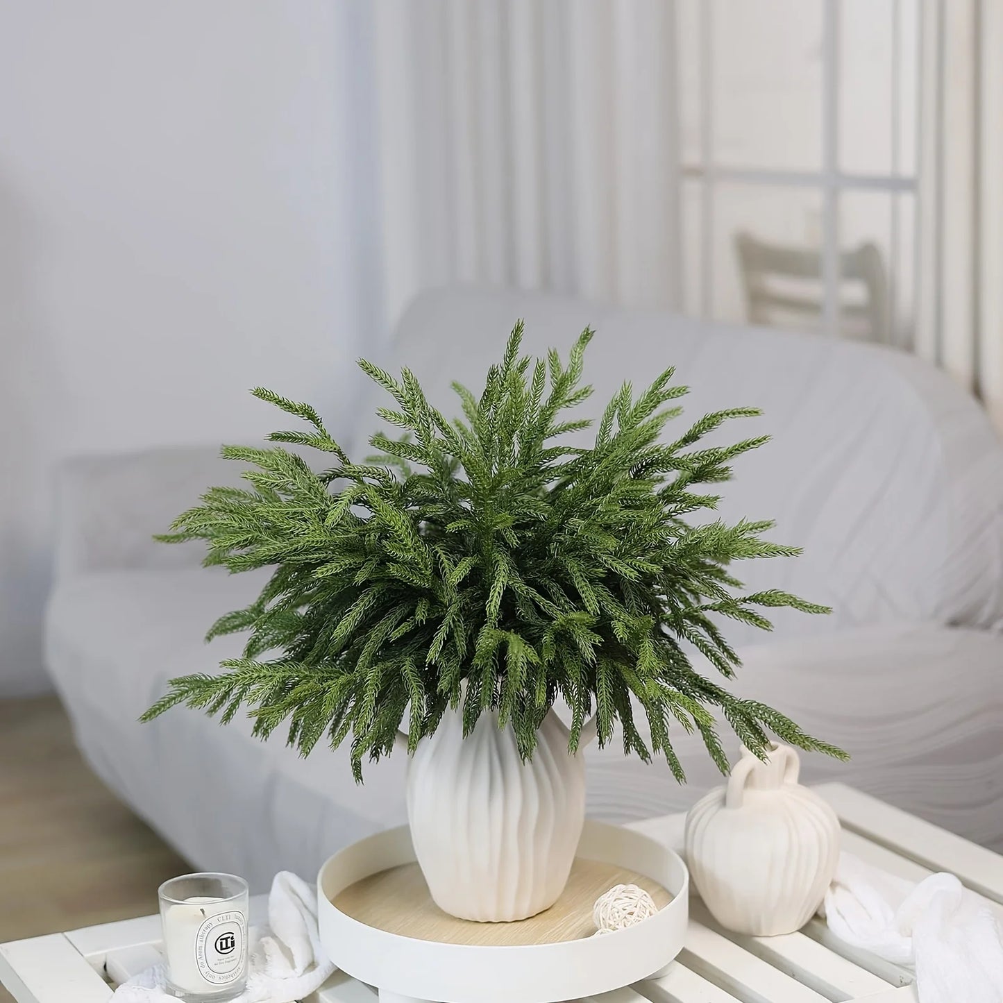 Decorative arrangement of real touch faux pine branches in a white ceramic vase on a living room table
