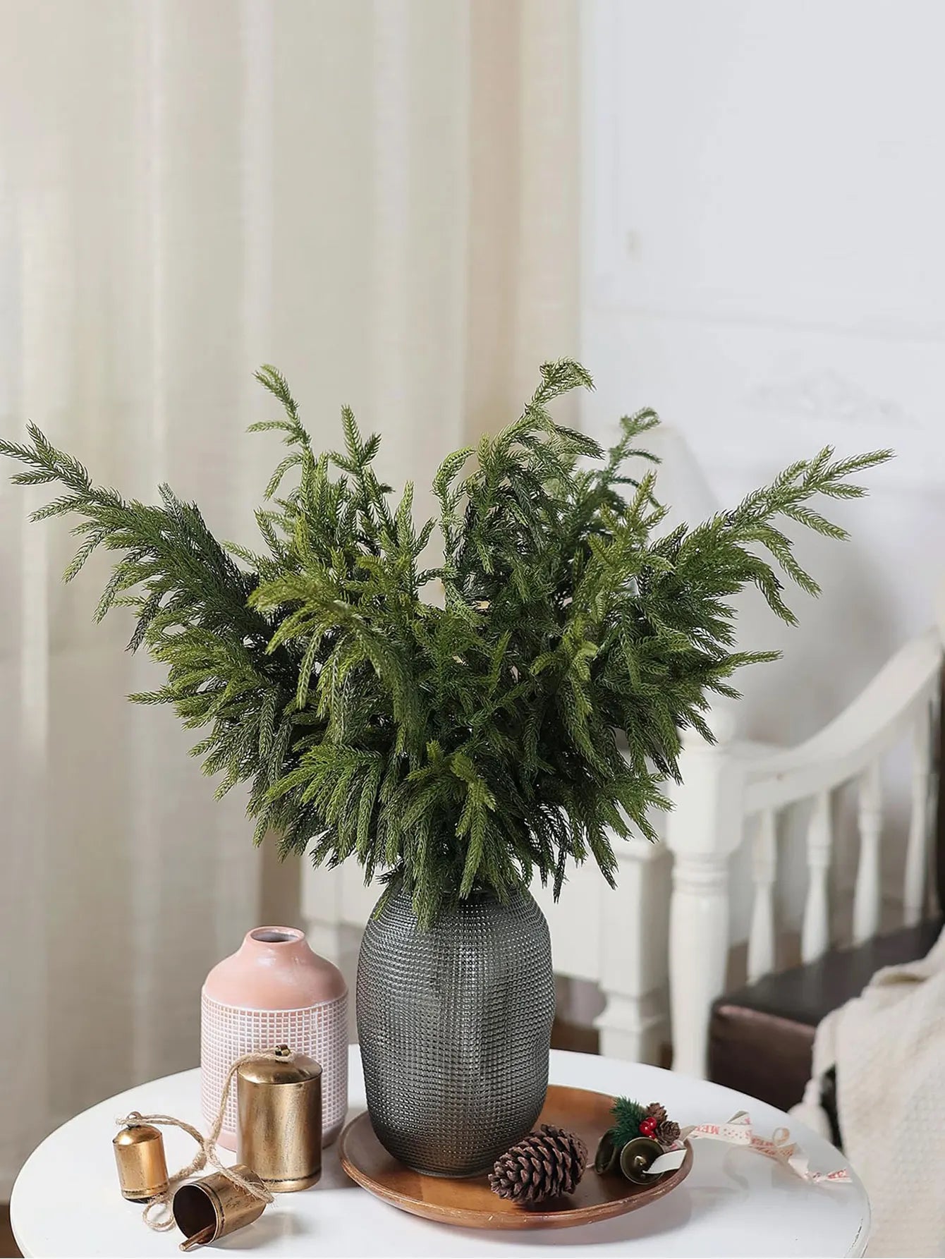 Real touch faux pine branches in a decorative vase with a cozy interior backdrop