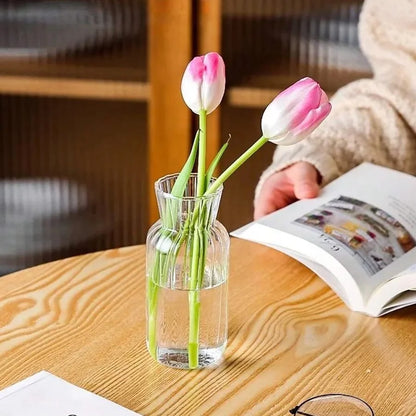 Nutshell transparent glass vase for flowers with pink tulips, displayed on a wooden table