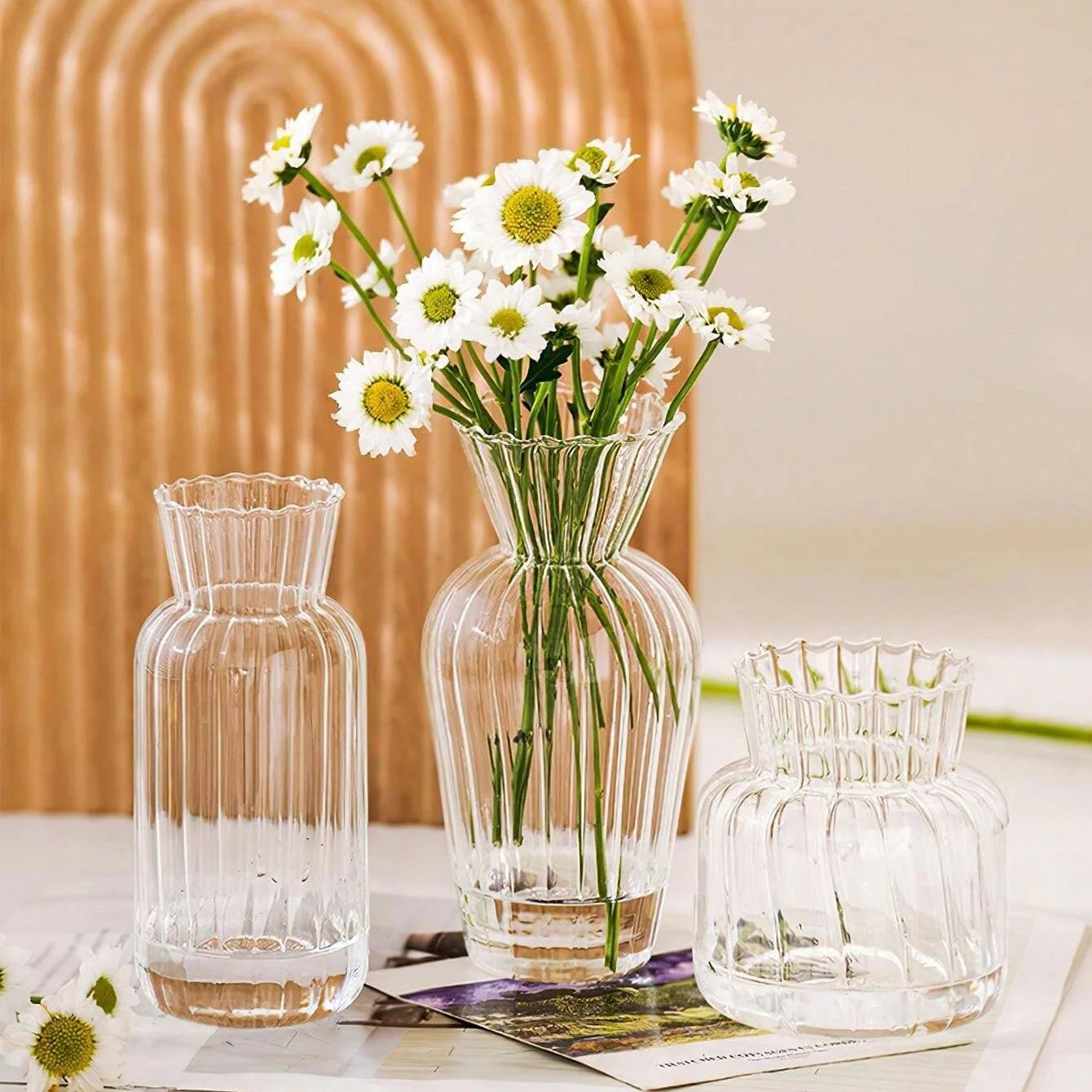 Three elegant transparent glass vases for flowers with unique designs and fresh flowers arranged inside